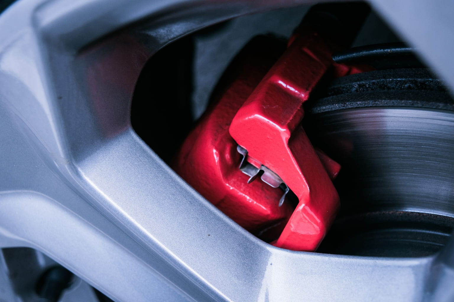 Red brake caliper over a brake disc, seen through the spokes of an alloy wheel