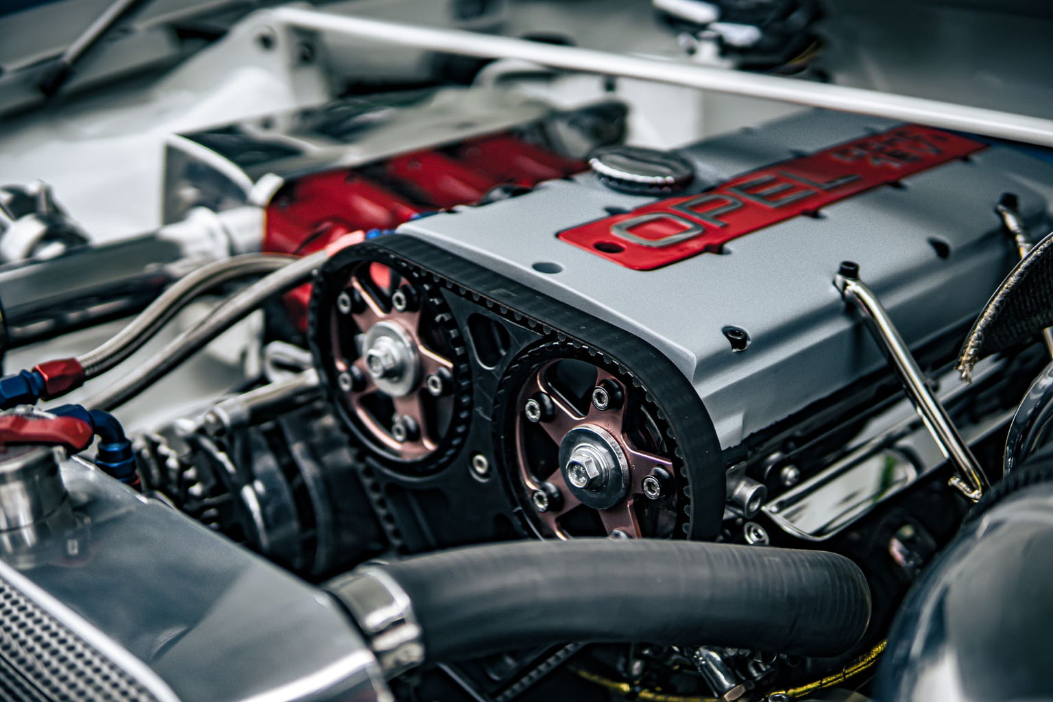 Car engine under the open hood with the red cam cover and timing gear visible