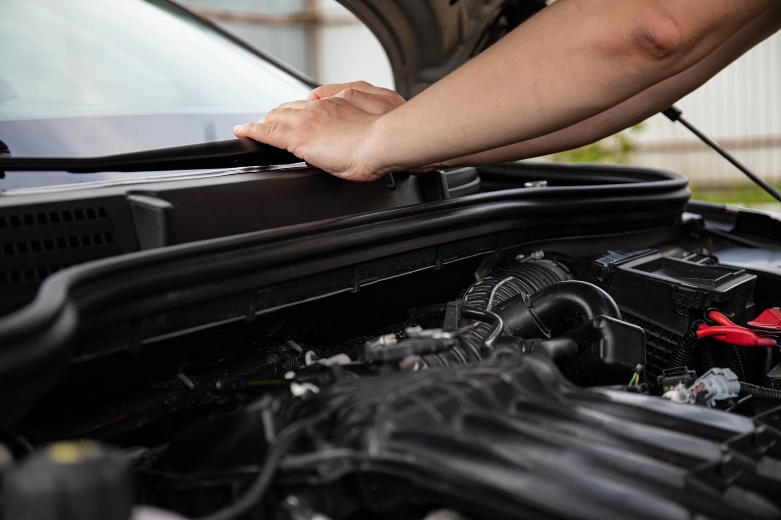 Hand resting on an open car hood above the engine bay