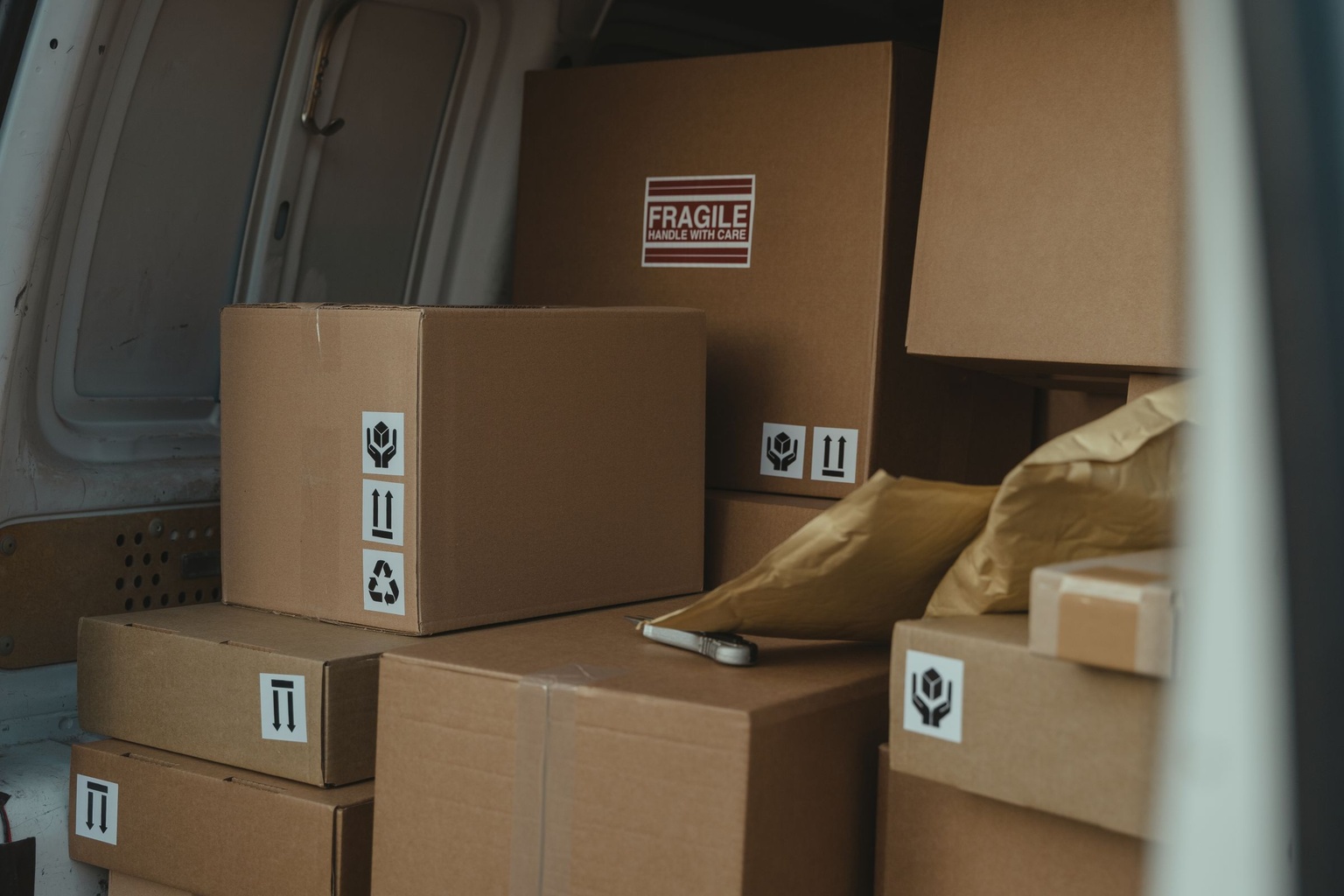 Cardboard parcels stacked in the cargo area of a delivery van, one marked fragile
