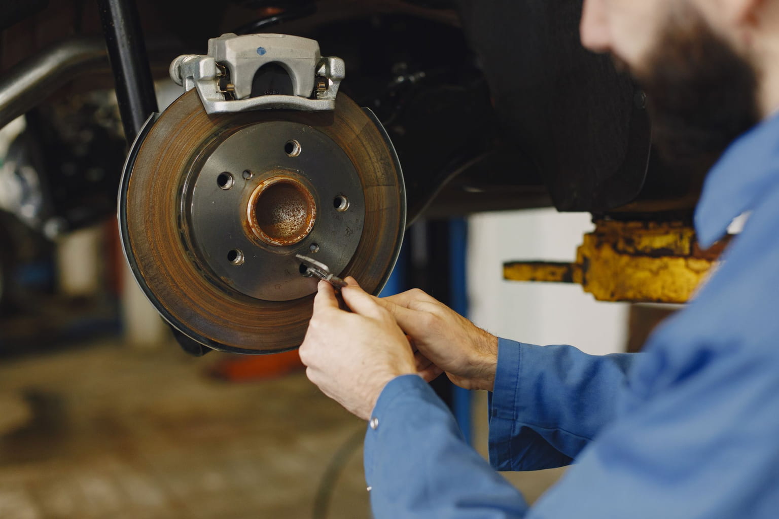 Mechanic working on a car's brake disc and caliper with the wheel removed