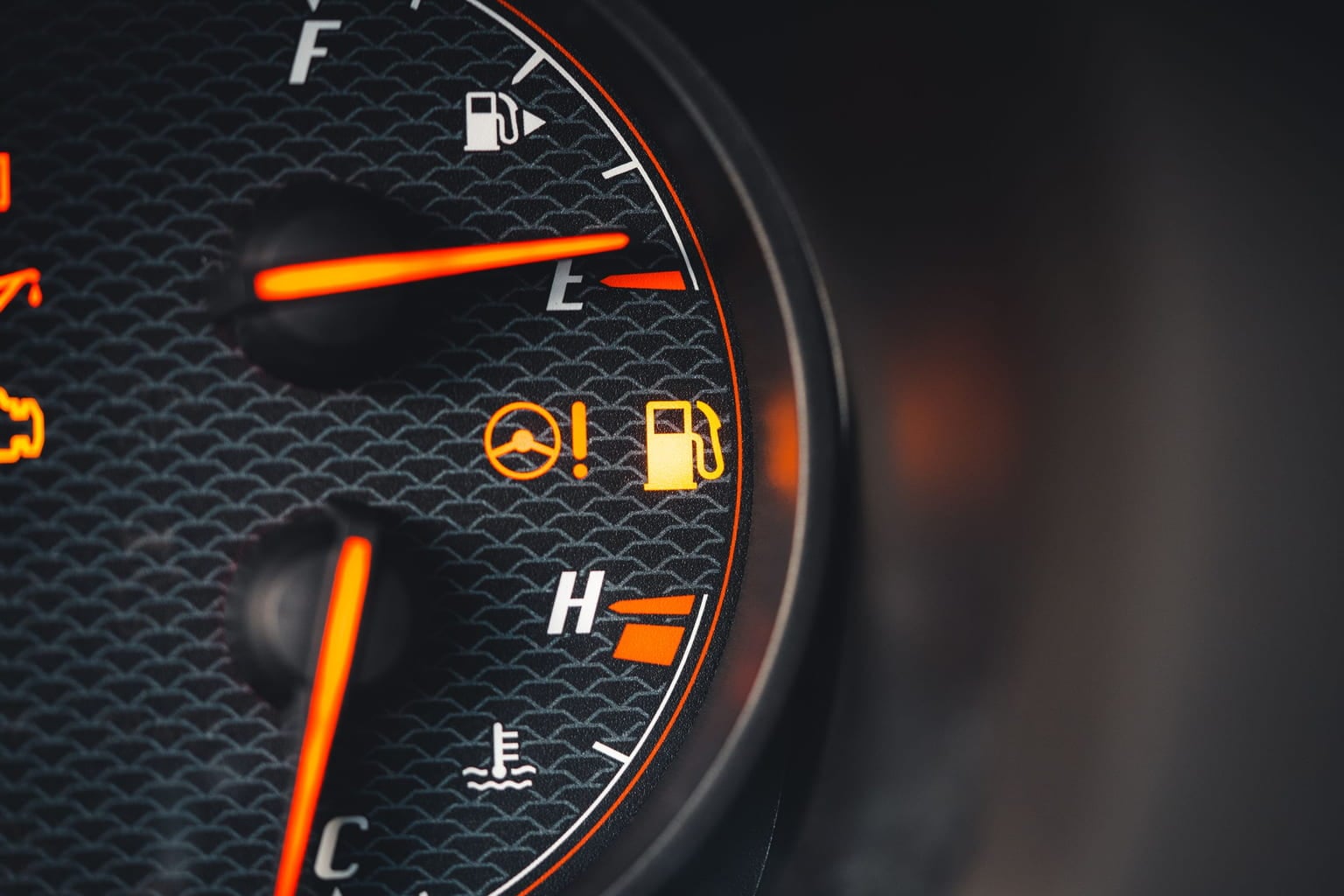 Amber warning lights glowing on a car's fuel and temperature gauges
