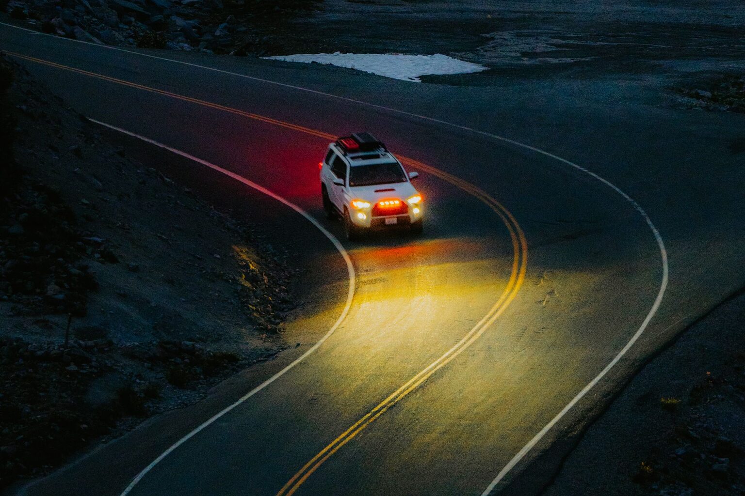 A white SUV with headlights on rounding a curve on a wet two-lane road at night