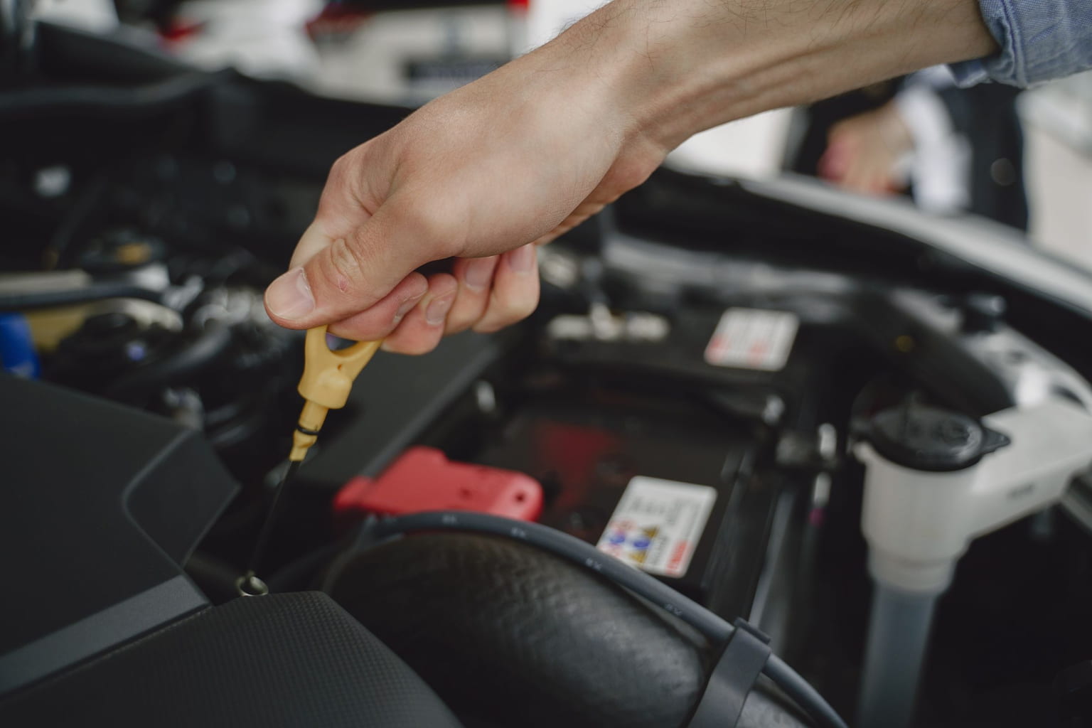 Hand pulling the yellow engine oil dipstick from a car engine