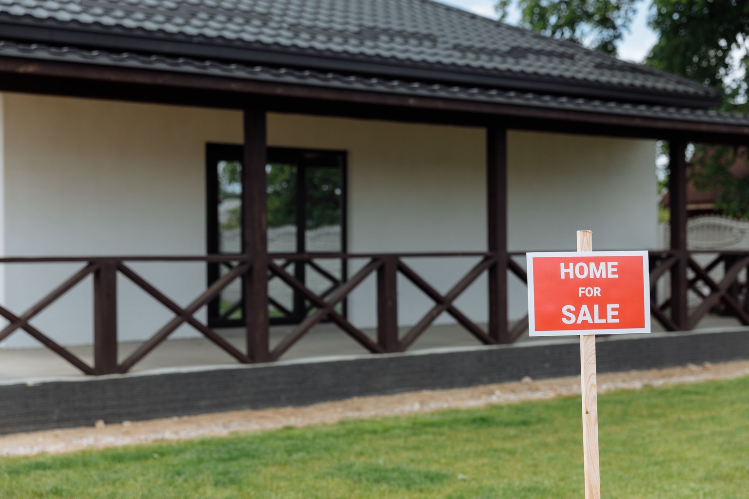 A red home for sale sign on a wooden post on the lawn of a single-storey house