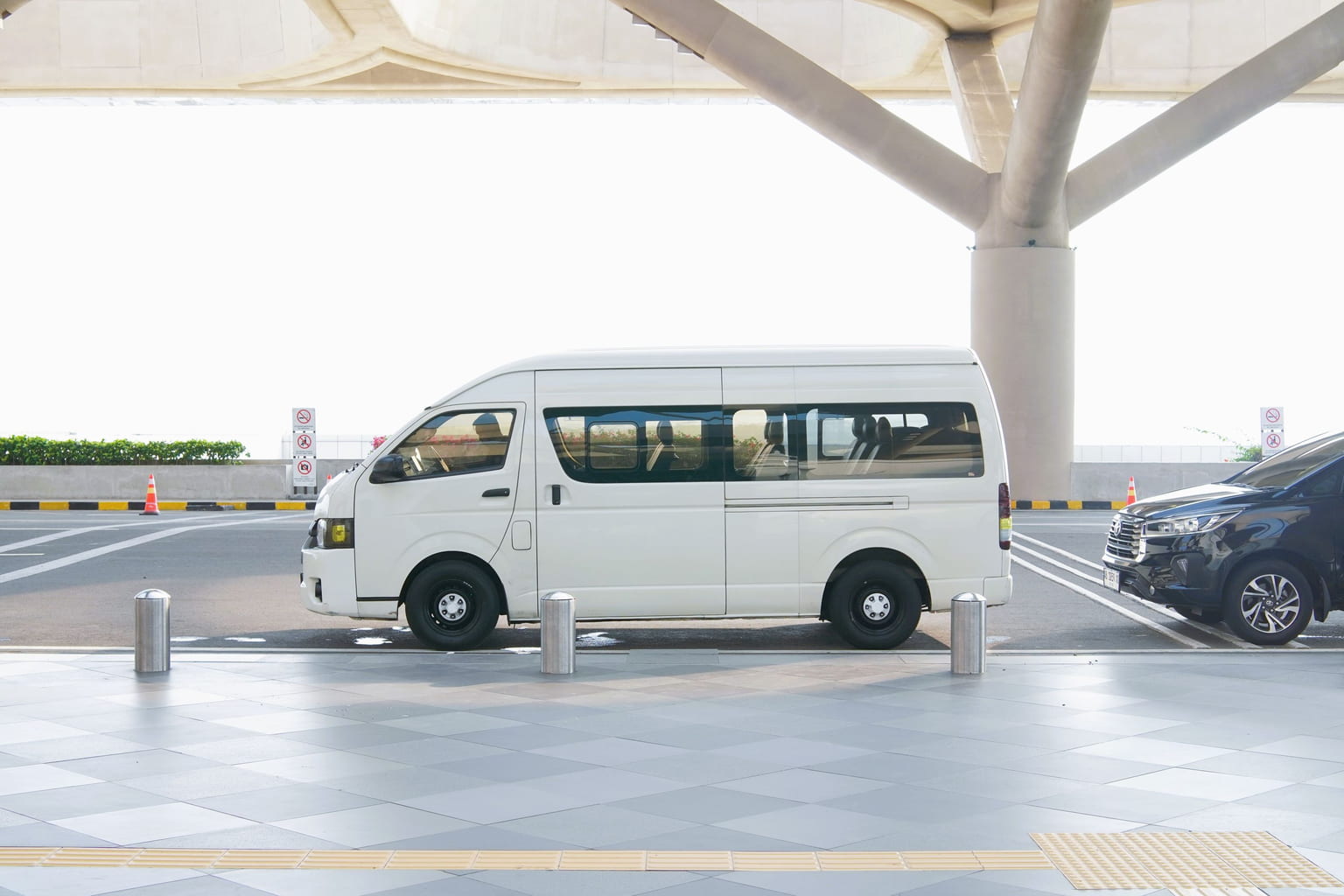 White passenger van parked at the drop-off kerb outside an airport terminal