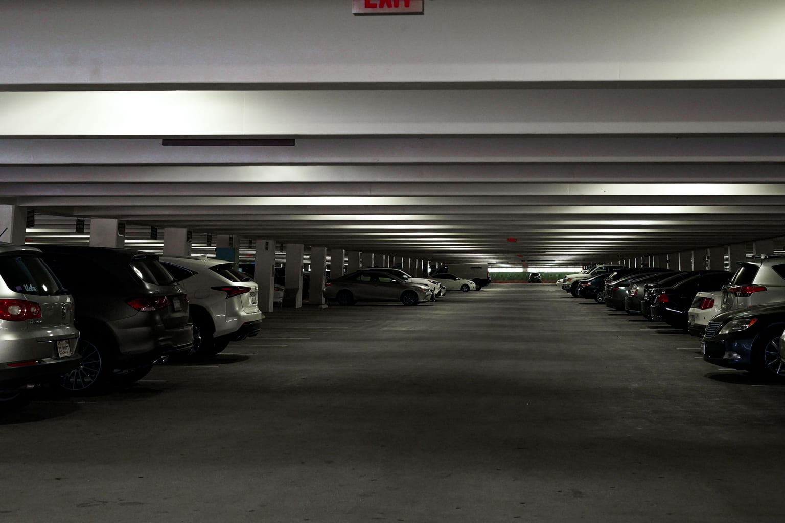 Inside a covered multi-level parking garage with cars parked along both sides