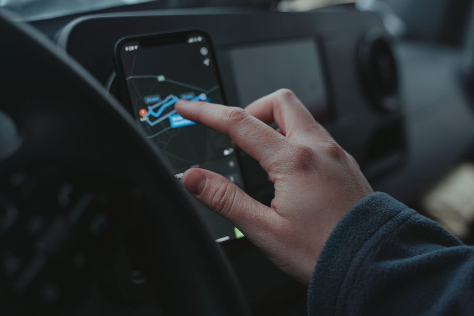 Driver's hand tapping a map app on a smartphone mounted in a car