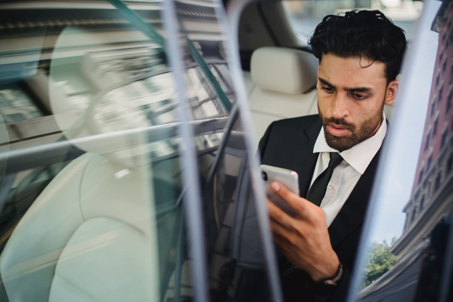 Businessman in a suit checking his smartphone in the back of a car