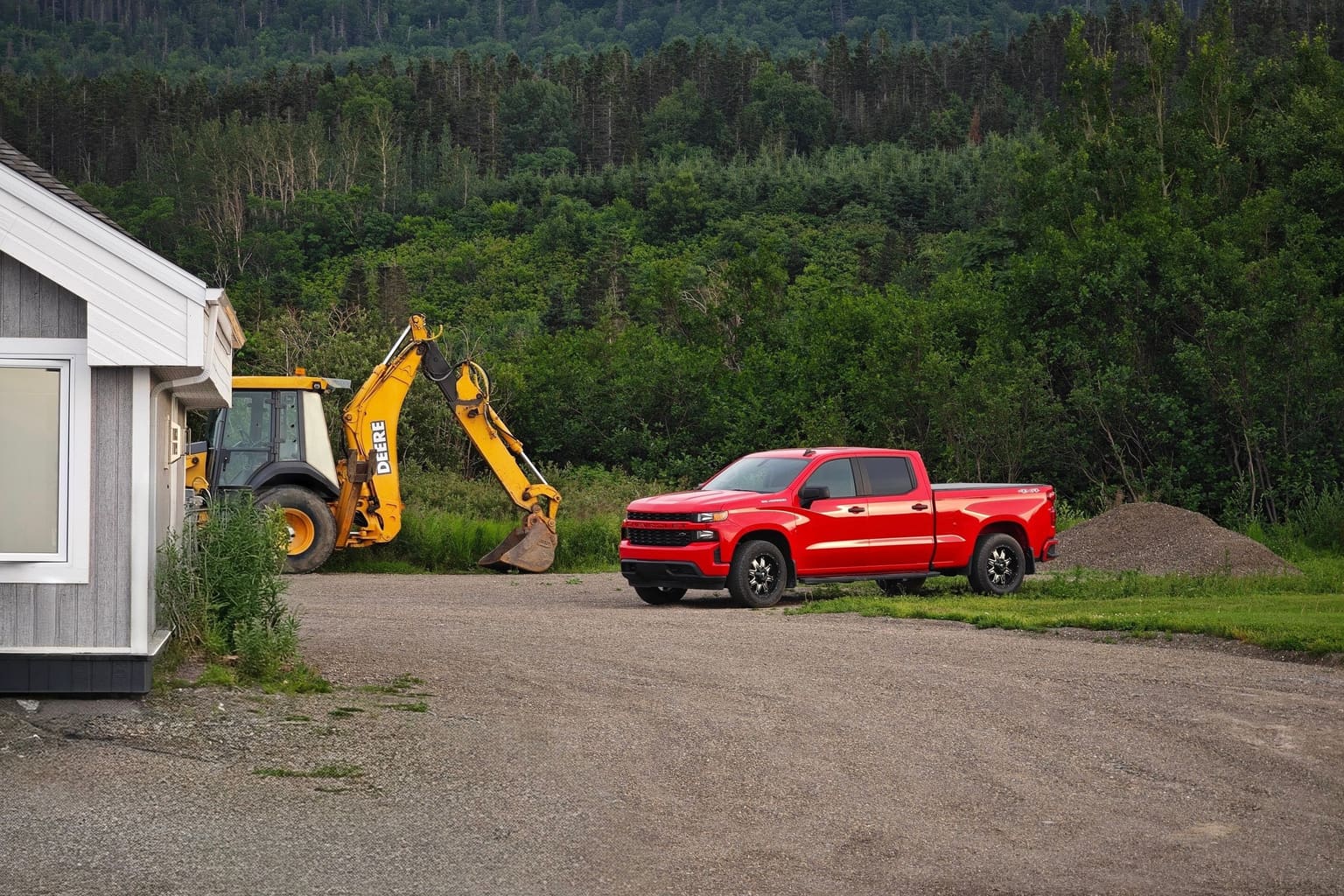 Red pickup truck parked beside a yellow backhoe on a gravel job site