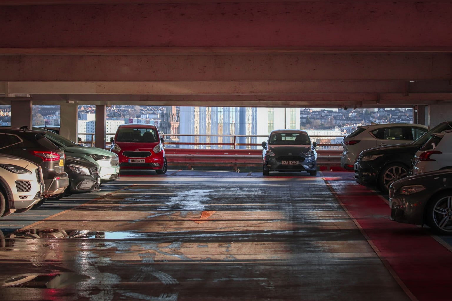 Cars parked on an upper level of a multi-storey garage with a city skyline beyond