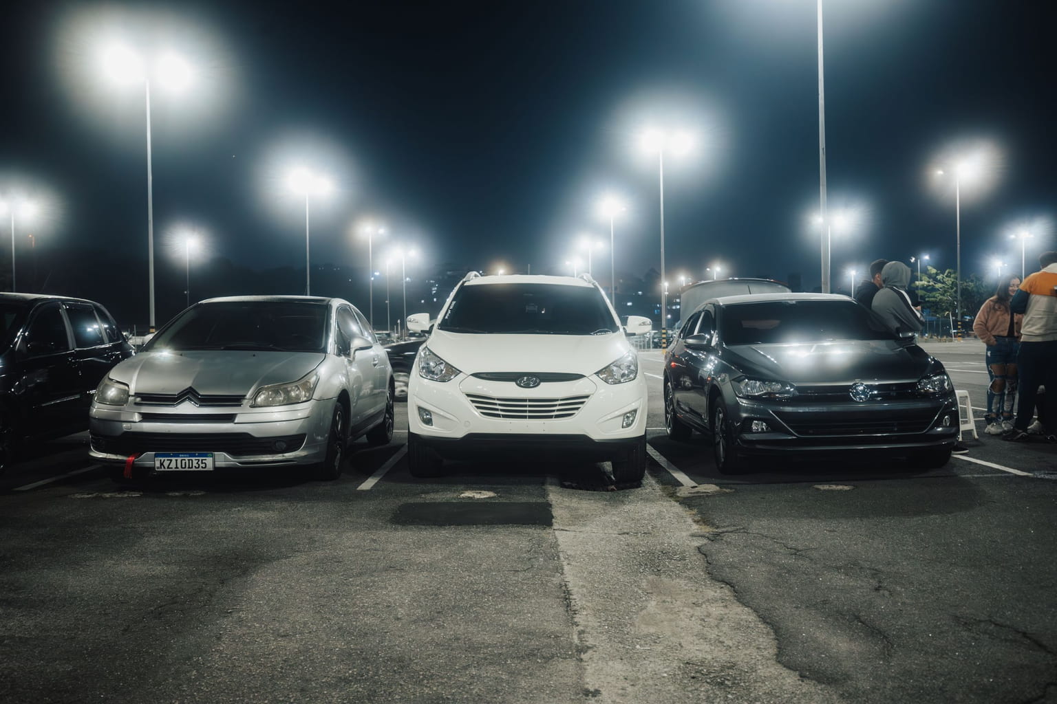 Cars parked under bright floodlights in an outdoor lot at night